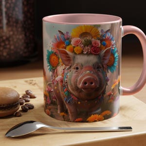 Puede incluir: Una taza de cerámica rosa con un diseño floral colorido que presenta un cerdo con una corona de flores. El cerdo está rodeado de flores y mariposas.