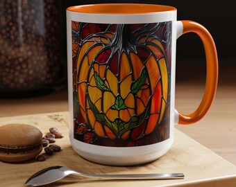 Könnte beinhalten: Weißer Keramikbecher mit orangefarbenem Innenraum und Henkel. Der Becher zeigt ein Design im Stil eines Glasfensters mit einem grinsenden Kürbis. Der Kürbis ist hauptsächlich orange und gelb mit grünen Blättern.