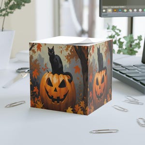 May include: A square notepad with a Halloween illustration. It shows a black cat sitting on a carved orange pumpkin, with autumn leaves and trees in the background. The design creates a spooky, seasonal atmosphere, perfect for autumn.