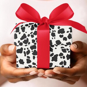 May include: A person is holding a gift box wrapped in black and white cow print paper with a red ribbon.