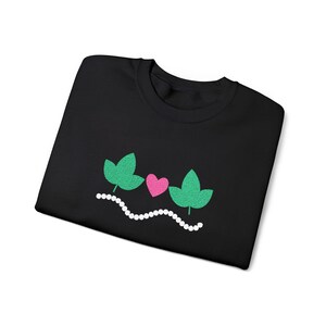 May include: Black sweatshirt featuring an embroidered design. The design includes two green leaves, a pink heart, and a white beaded line. The sweatshirt is made of a soft material and is suitable for casual wear.