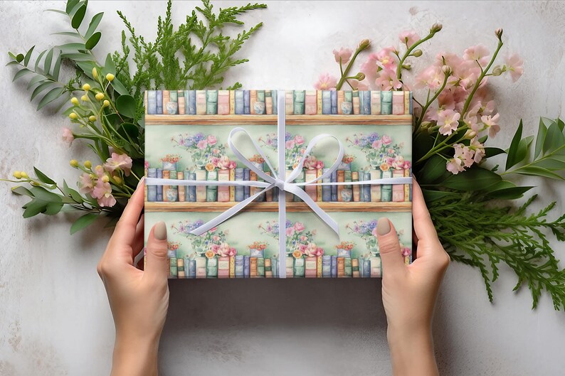 May include: A gift wrapped in white paper with a white ribbon. The paper has a pattern of books on shelves with flowers.