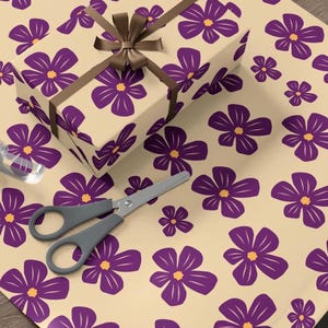 May include: A sheet of beige wrapping paper with a repeating pattern of purple flowers with yellow centres. A brown ribbon is tied around a gift box wrapped in the same paper.