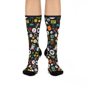 May include: A pair of black socks with a colorful science-themed pattern. The socks feature various science-related icons, including atoms, test tubes, light bulbs, and the equation E=mc².