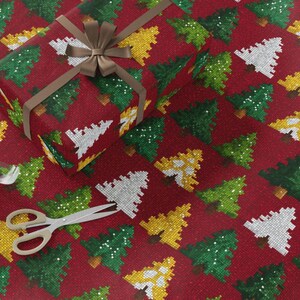 May include: A wrapped gift box with a brown ribbon and bow sits on a red wrapping paper background. The wrapping paper and gift box feature a repeating pattern of pixelated Christmas trees in white, green, and yellow.