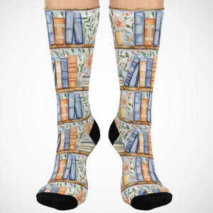 May include: A pair of knee-high socks featuring a repeating pattern of bookshelves with blue and orange books. The background has a floral design with orange flowers and green leaves. The socks have black heels and toes.