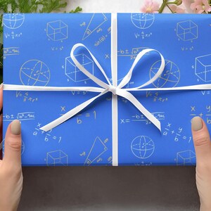 May include: A blue gift box wrapped in paper with a white ribbon. The paper has a pattern of white mathematical equations and geometric shapes.