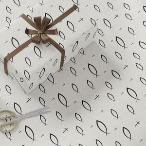 May include: A wrapped gift box with a brown ribbon and bow sits on white wrapping paper. The paper has a repeating pattern of black fish symbols and crosses. A pair of scissors with gold handles is in the lower left corner.