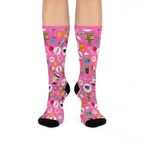 May include: Pink socks with a science theme. The socks feature a variety of science-related icons, including atoms, molecules, test tubes, and beakers. The socks also feature the equation E=mc2.