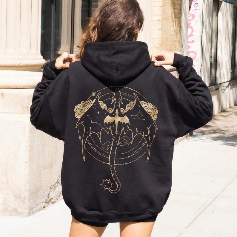 May include: Black hooded sweatshirt with a gold dragon graphic on the back. The dragon design includes wings, a tail, and celestial elements. The sweatshirt is a casual style.