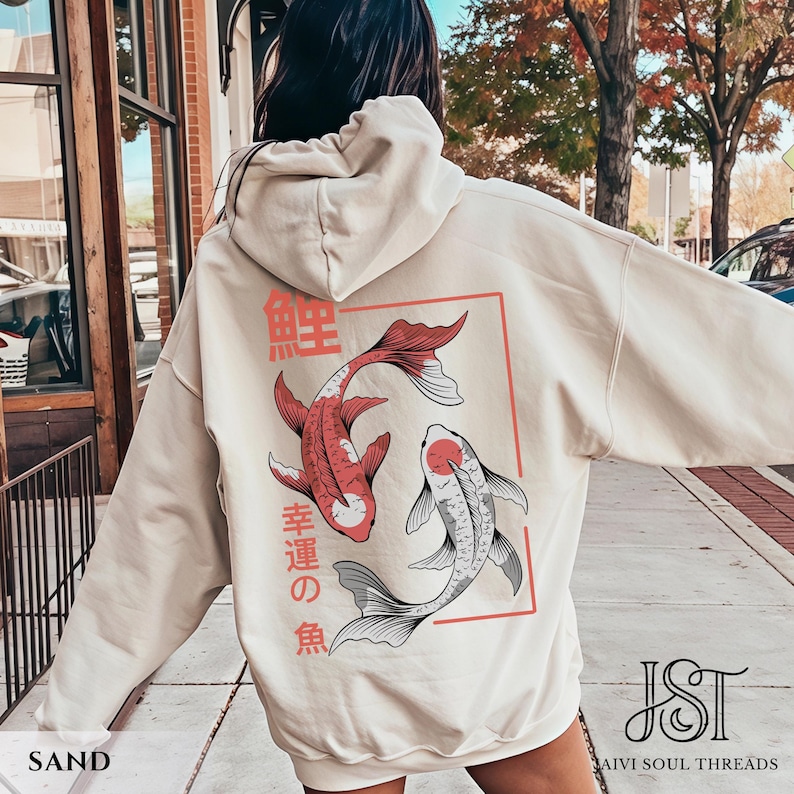 May include: Sand-colored hoodie featuring a Japanese koi fish design. The back of the hoodie displays two koi fish in red and gray, with Japanese text above and below. The hoodie has a drawstring hood and a kangaroo pocket.