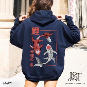 May include: Navy blue hoodie featuring a red and white koi fish design within a red rectangular frame. Japanese characters are above and to the side of the fish. The hoodie has a drawstring hood and long sleeves. The text "NAVY" is at the bottom.