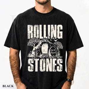 May include: Black t-shirt with a distressed graphic design. The design features the words "ROLLING STONES" above an illustration of a tomb with a cross, trees, and birds. The text "He is Risen! Since AD 33" is also included.