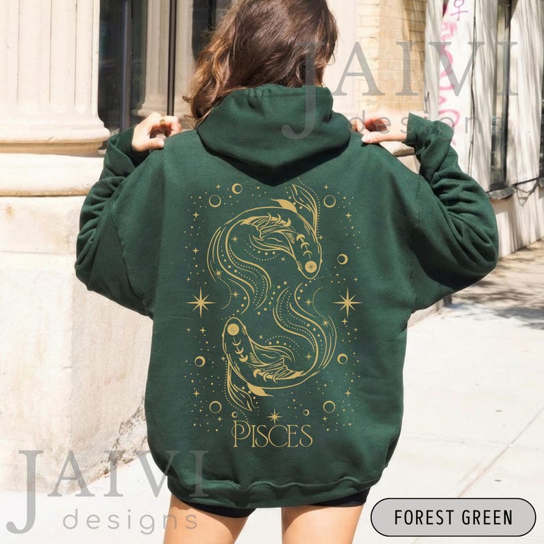 K&ouml;nnte beinhalten: Forstgr&uuml;ner Kapuzenpullover mit goldenem Fische-Design auf dem R&uuml;cken. Das Design umfasst zwei stilisierte Fische, Sterne und das Wort "PISCES". Der Hoodie hat eine Kapuze mit Kordelzug und eine K&auml;ngurutasche.