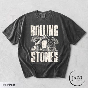 May include: Pepper-colored t-shirt with a distressed graphic. The design features the words "ROLLING STONES" in a bold, textured font, with an illustration of a tomb and cross. The text "He is Risen! Since AD 33" is also included.