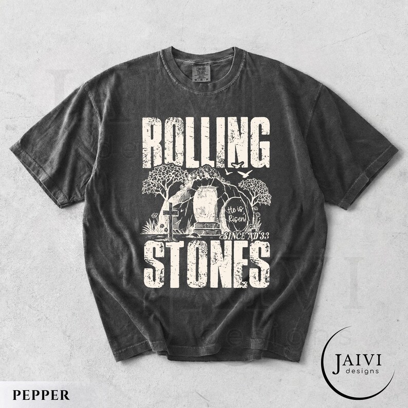 May include: Pepper-colored t-shirt with a distressed graphic. The design features the words "ROLLING STONES" in a bold, textured font, with an illustration of a tomb and cross. The text "He is Risen! Since AD 33" is also included.