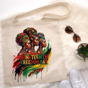 May include: A beige tote bag featuring a vibrant illustration of three women wearing colorful head wraps and jewelry. The text "Juneteenth Freedom Day" is displayed in bold, colorful letters. The design incorporates red, green, and yellow paint drips.