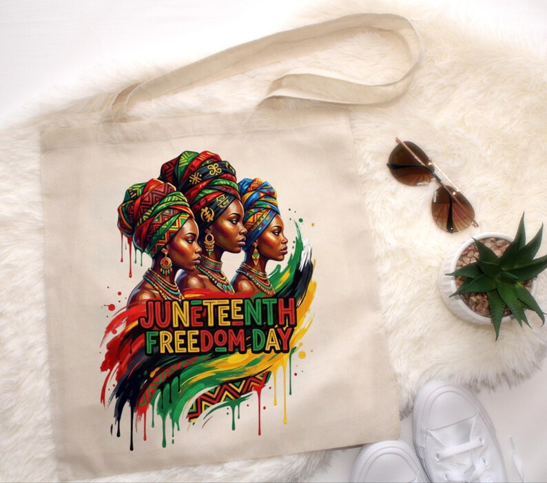 May include: A beige tote bag featuring a vibrant illustration of three women wearing colorful head wraps and jewelry. The text "Juneteenth Freedom Day" is displayed in bold, colorful letters. The design incorporates red, green, and yellow paint drips.