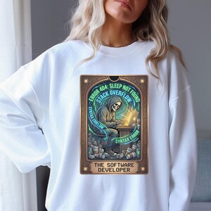 Puede incluir: Sudadera blanca con un gráfico de un esqueleto con capucha trabajando en una computadora portátil. El gráfico incluye el texto "ERROR 404: SLEEP NOT FOUND, STACK OVERFLOW, SYNTAX ERROR" y "THE SOFTWARE DEVELOPER".