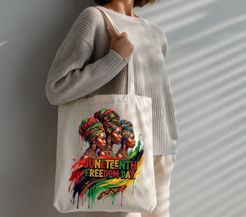 May include: A cream-colored tote bag featuring a vibrant illustration of three women wearing colorful head wraps. The design includes the text "Juneteenth Freedom Day" with a colorful paint stroke design.