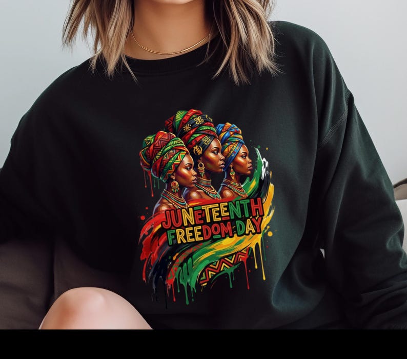 May include: Black sweatshirt featuring a colorful graphic of three women wearing head wraps, with the text "Juneteenth Freedom Day" in red, yellow, and green. The design incorporates the colors of the Pan-African flag.