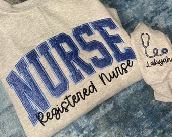 May include: A gray sweatshirt with the word "NURSE" in blue glitter lettering and the words "registered nurse" written in black cursive. The sweatshirt has a matching blue stethoscope and the name "Lakiyah" embroidered on the sleeve.