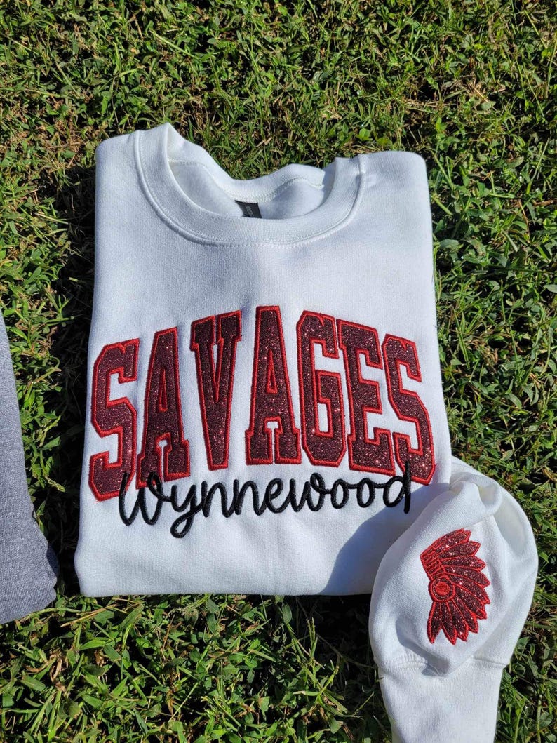 May include: White sweatshirt with red glitter lettering that says "SAVAGES Wynnewood" and a red glitter Native American headdress on the sleeve.