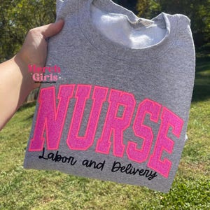 Puede incluir: Sudadera gris con letras de purpurina rosa que dicen "NURSE Trabajo y Parto".