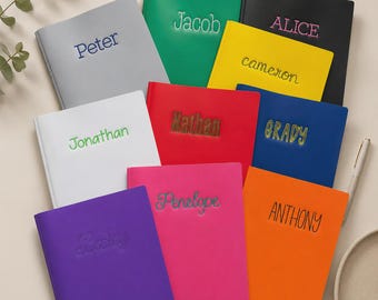 Può includere: Una collezione di undici quaderni rettangolari in vari colori a tinta unita, tra cui grigio, verde, nero, giallo, bianco, rosso, blu, viola, rosa e arancione. Ogni quaderno presenta un nome unico ricamato o stampato sulla copertina.