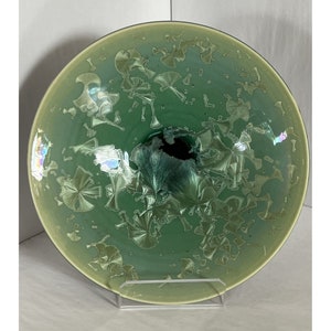 May include: A large, round, green ceramic plate with a textured, iridescent glaze. The plate has a raised center and a wide, flat rim.