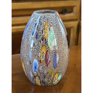 May include: A clear glass vase with a textured surface and colorful confetti-like designs. The vase is oval shaped and has a wide opening.