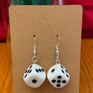 May include: A pair of white dice earrings with black dots. The dice are hanging from silver earring hooks.