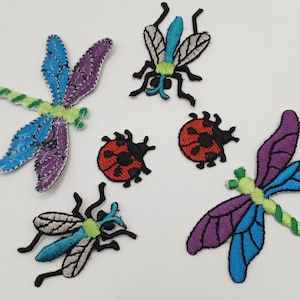 Könnte beinhalten: Fünf gestickte Bügelbilder mit Insekten und Marienkäfern. Die Patches beinhalten eine blaue und violette Libelle, eine grüne und blaue Libelle, eine grüne und blaue Fliege und zwei rote Marienkäfer.
