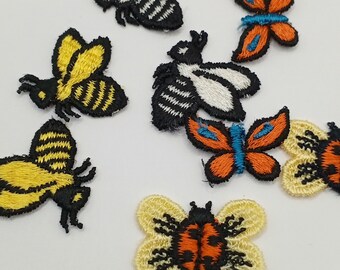 May include: Assortment of embroidered iron-on patches featuring various insects, including bees, butterflies, and ladybugs. The patches are in shades of yellow, black, orange, red, blue, and white.