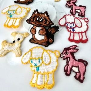 May include: Assortment of embroidered iron-on patches featuring various animals, including a lamb, a donkey, a raccoon, and a deer. The patches are in various colors, including pink, brown, white, and yellow.