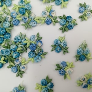 May include: Assortment of blue and green fabric flower embellishments. Each flower is made of a cluster of small blue fabric flowers with green fabric leaves.