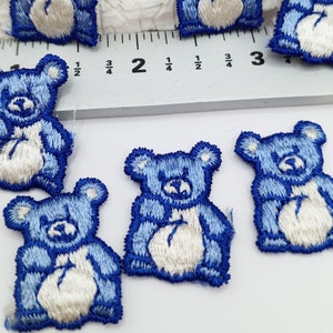 May include: Blue embroidered teddy bear iron-on patches. The bears are approximately 1 inch tall and have white faces and bellies.