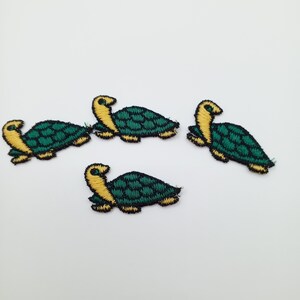 Könnte beinhalten: Vier gestickte Schildpattenstickereien in Grün und Gelb. Die Schildkröten haben eine grüne Schale und einen gelben Kopf und Beine.