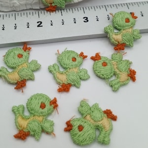 May include: Six green and yellow embroidered felt appliques of ducks with orange beaks and feet. The ducks are approximately 1 inch in size.