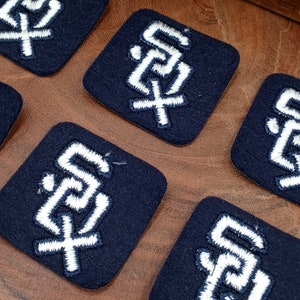 May include: Five navy blue felt patches with white embroidered letters spelling out "S.F." in a stylized font.