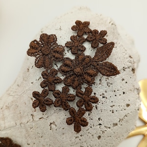 May include: Brown lace applique with a floral design. The lace is made of delicate fabric and features intricate details.