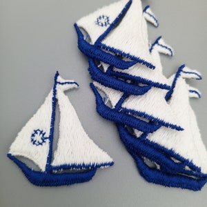 May include: A set of ten white felt sailboat appliques with blue trim. The sailboats are approximately 2 inches tall.