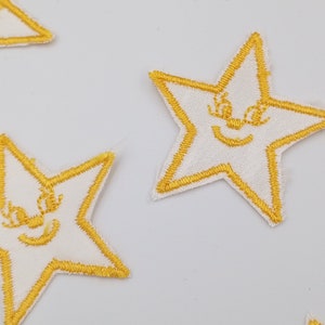 Könnte beinhalten: Fünf weiße Stoff-Stern-Patches mit gelben gestickten Umrissen und lächelnden Gesichtern.