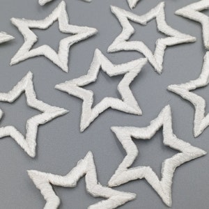 May include: A collection of white, embroidered star-shaped patches. The stars are outlined in white thread and have a slightly raised texture.
