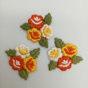 May include: Three embroidered flower appliques in orange, yellow, and white. The flowers are arranged in clusters of three and have a vintage style.