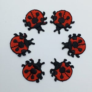 May include: Six embroidered ladybug patches. Each patch features a red body with black spots and a black outline. The ladybugs are arranged in a circular pattern against a white background. These patches are ideal for adding to clothing or accessories.
