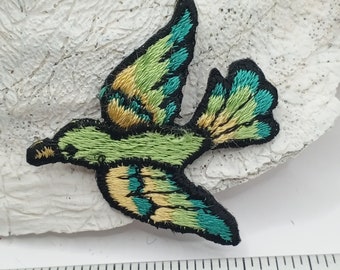 Puede incluir: Parche de aplique de pájaro bordado en verde y azul. El pájaro está volando con las alas extendidas. El parche mide aproximadamente 5 cm de largo.