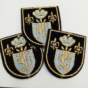 May include: Three black velvet patches with gold and light blue embroidery. Each patch features a coat of arms with a crown, a lion, and floral accents.