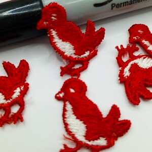 May include: Four red felt bird appliques with white accents. The birds are embroidered with a simple design and have a slightly 3D appearance.