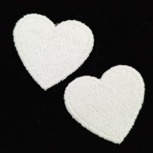 May include: Two white felt heart-shaped patches. The hearts are stitched with a white thread and have a slightly textured surface.
